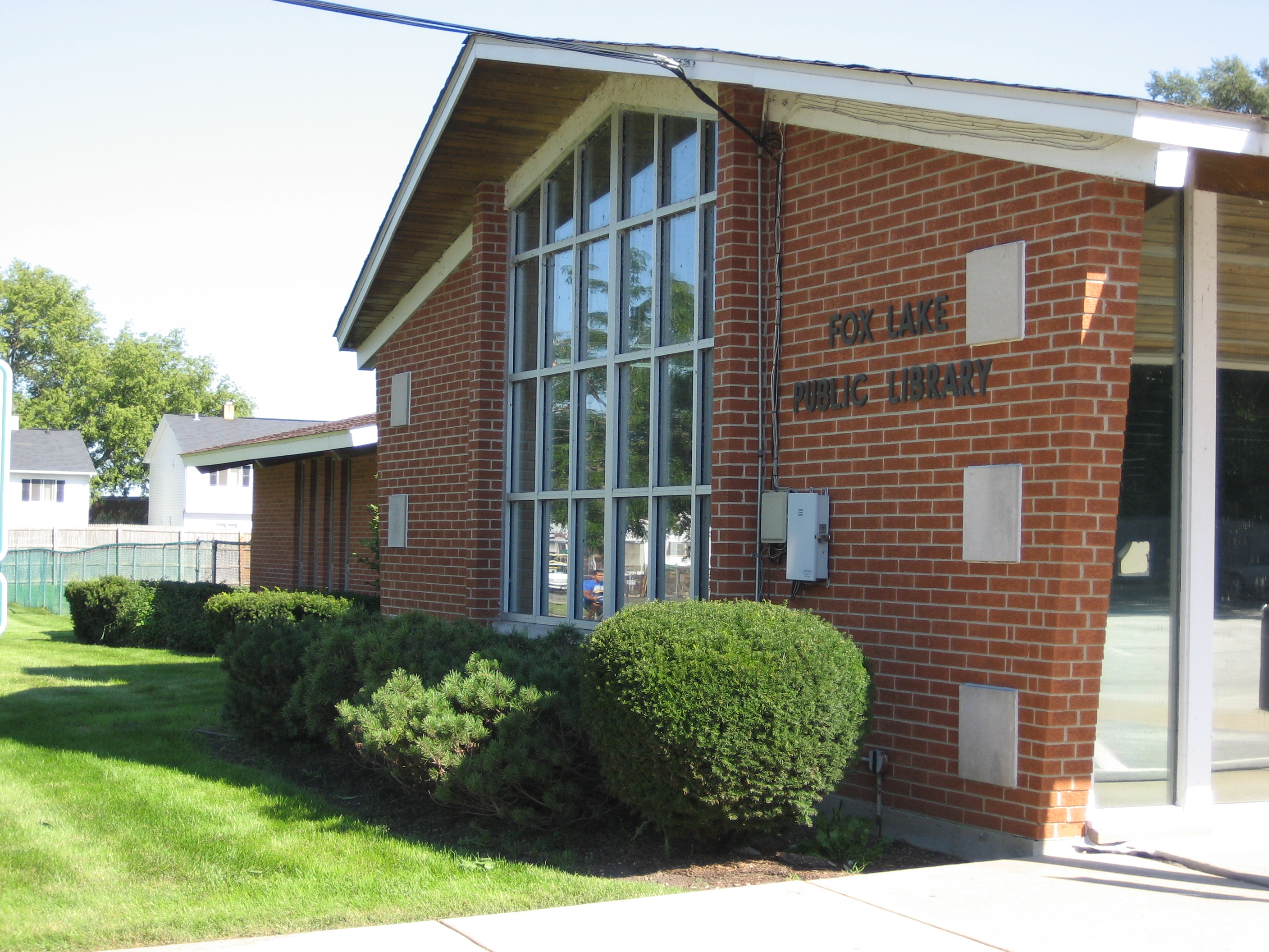 Original library close up of windows, "Fox Lake Public Library" metal sign, and landscaping