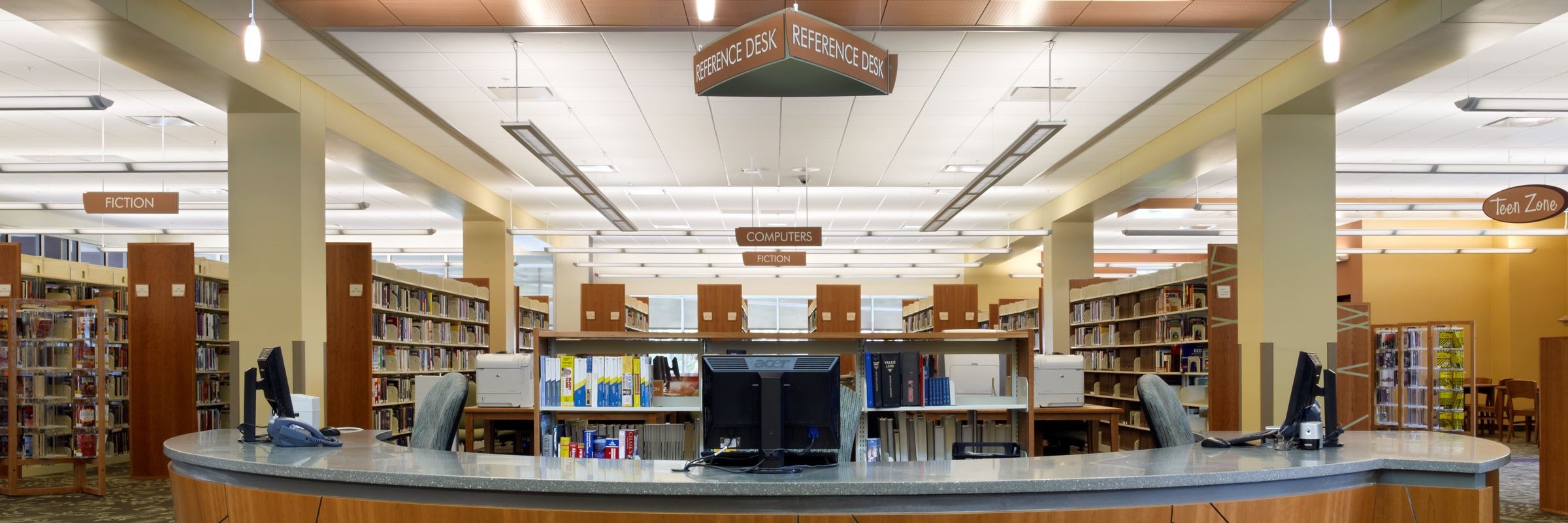 Interior library photo centered on circular reference desk with shelving and signs behind
